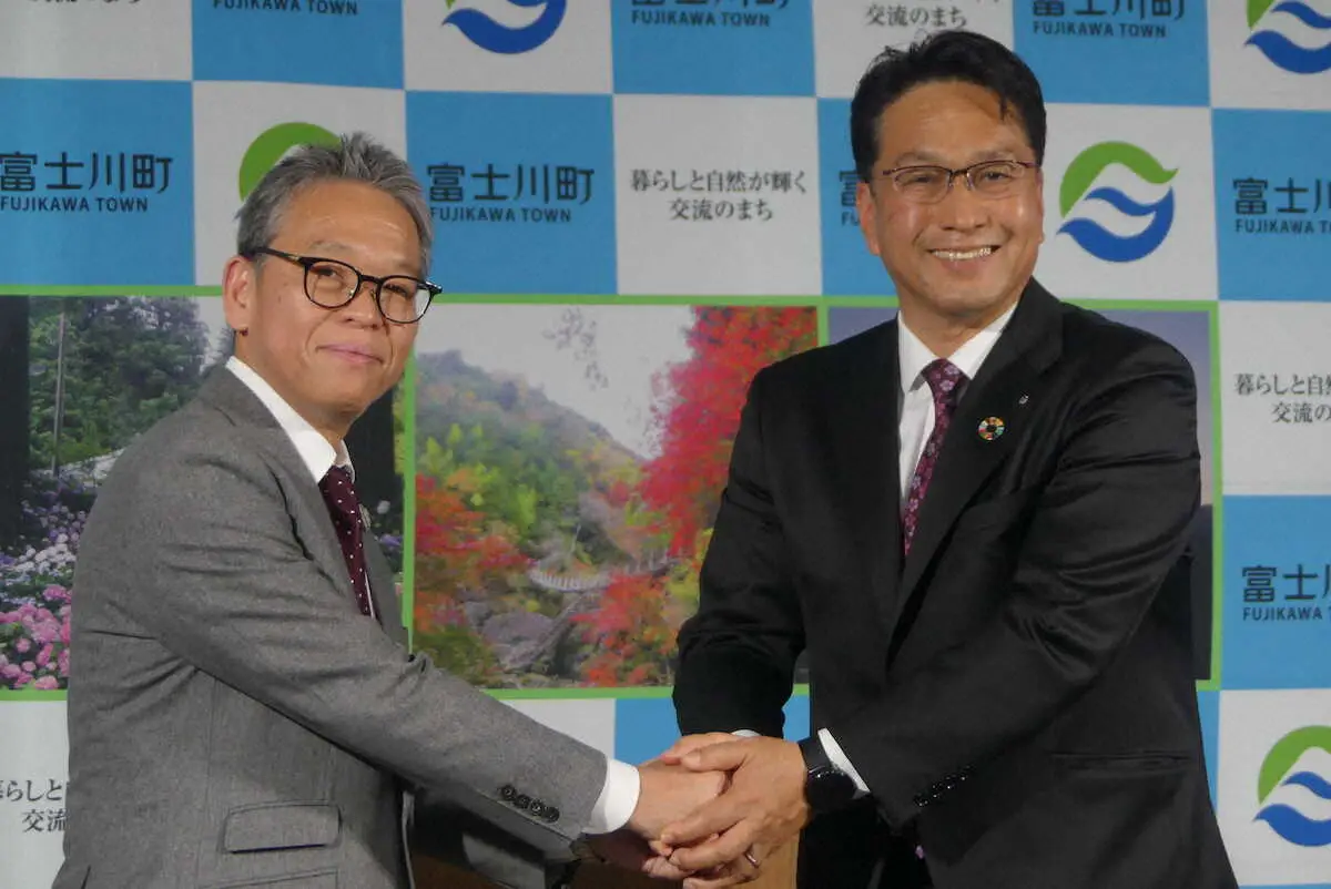 オフィシャルパートナー協定を締結し握手する菅井敦社長（左）と望月利樹町長